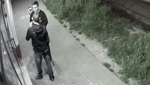 zdjęcie czarno-białe: młody mężczyzna, podejrzany o kradzież torby, rozmawiający pod sklepem z innym mężczyzna