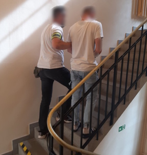 zdjęcie kolorowe: policjant kryminalny prowadzący zatrzymanego mężczyznę po schodach