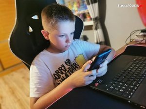 zdjęcie kolorowe: chłopiec siedzący przed komputerem i korzystający z telefonu komórkowego