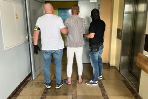 zdjęcie kolorowe: dwóch policjantów wydziału kryminalnego z zatrzymanym mężczyzna podejrzanym o zabójstwo kolegi