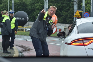 4 - zdjęcie kolorowe: mężczyzna odpowiedzialny za bezpieczeństwo na trasie ze strony organizatora rozmawiający z policjantem siedzącym w nieoznakowanym radiowozie
