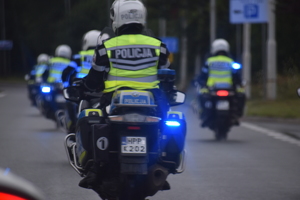 18 -  zdjęcie kolorowe: policjanci ruchu drogowego jadący na służbowych motocyklach po trasie wyścigu