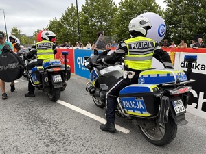 23 - zdjęcie kolorowe: policjanci ruchu drogowego na motocyklach oczekujący na kolarza i wpuszczanie na trasę wyścigu