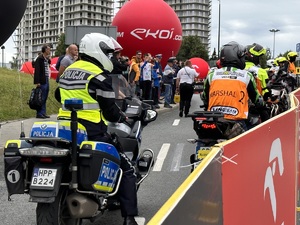 24 - zdjęcie kolorowe: policjanci ruchu drogowego na motocyklach oczekujący na kolarza i wpuszczanie na trasę wyścigu