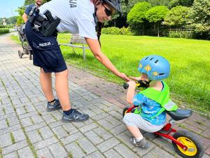 Zdjęcie kolorowe przedstawia policjanta &quot;zbijającego piątkę&quot; z dzieckiem na rowerze.
