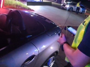 Zdjęcie kolorowe przedstawia policjanta na tle zaparkowanego samochodu.