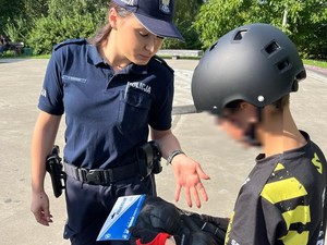 Zdjęcie kolorowe przedstawiające policjantkę wręczającą komplet ochraniaczy dziecku w skateparku.