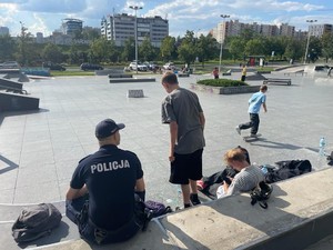 Zdjęcie kolorowe przedstawia policjanta podczas rozmowy z osobami korzystającymi ze skateparku.