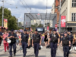 zdjęcie kolorowe: umundurowani policjanci nadzorujący przemarsz uczestników zgromadzenia w centrum Katowic