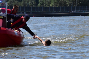 zdjęcie kolorowe; policjant i ratownik wodny na motorówce współpracujący przy wyciąganiu pozoranta z wody