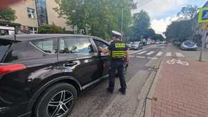 zdjęcie kolorowe: policjant ruchu drogowego kontrolujący pojazdy w rejonie szkoły
