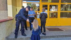 zdjęcie kolorowe: policjant i strażnicy miejscy rozdający uczniom elementy odblaskowe