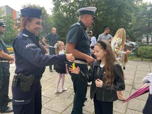 zdjęcie kolorowe: policjantka i inspektor inspekcji transportu drogowego rozdający odblaski pierwszoklasistom
