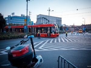 Zdjęcie kolorowe przedstawia na pierwszym tle policyjny motocykl, w drugim planie widać przejeżdżający na skrzyżowaniu tramwaj.