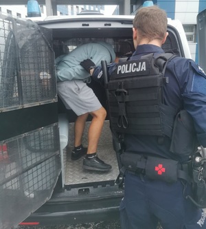 zdjęcie kolorowe: katowiccy policjanci podczas wyprowadzania  zatrzymanych pseudokibiców z radiwozou