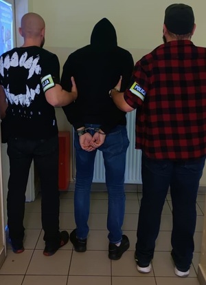 zdjęcie kolorowe: dwóch policjantów kryminalnych trzyma za ręce mężczyznę podejrzanego o rozbój