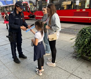 zdjęcie kolorowe: katowicka policjantka wręczający elementy  dziewczynce i jej matce