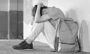 zdjęcie czarno-białe: siedzący na podłodze nastolatek, który opiera głowę o kolana