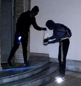 zdjęcie kolorowe: mężczyzna ubrany w ciemne spodnie, ciemna bluzę i czarną kominiarkę założoną na głowę na terenie posesji, z której ukradziono dwa rowery elektryczne