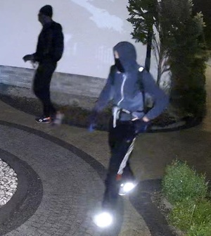 zdjęcie kolorowe: mężczyzna ubrany w ciemne spodnie, ciemna bluzę i czarną kominiarkę założoną na głowę na terenie posesji, z której ukradziono dwa rowery elektryczne