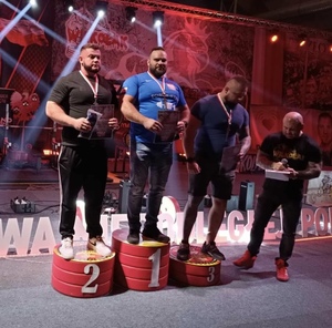 zdjęcie kolorowe: aspirant sztabowy Krzysztof Banaś stojący na pierwszym miejscu podium w towarzystwie dwóch zawodników