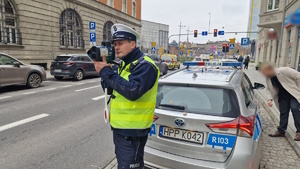 Zdjęcie kolorowe: policjant dokonujący pomiaru prędkości pojazdu