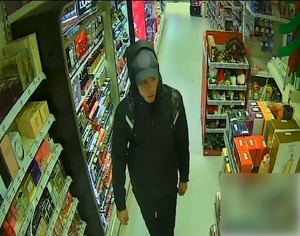zdjęcie kolorowe: przedstawiającego osobę podejrzewaną o kradzież perfum w drogerii. Mężczyzna ubrany w czarną kurtkę oraz czarną czapkę z daszkiem na głowie. Zdjęcie zarejestrowane przez sklepowy monitoring
