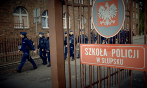 zdjęcie kolorowe: młodzi policjanci przechodzący przez bramę Szkoły Policji w Słupsku
