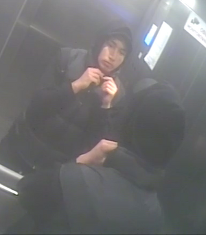 zdjęcie kolorowe: mężczyzna  przeglądający się w lustrze zamontowanym w windzie, ubrany w czarne spodnie i czarą kurtkę z kapturem