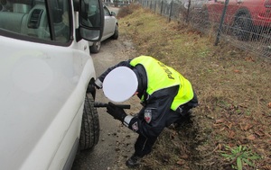 zdjęcie kolorowe: policjant wydziału ruchu drogowego sprawdzający stan techniczny samochodu