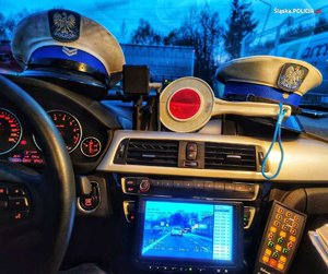 zdjęcie kolorowe: wnętrze policyjnego radiowozu, w którym znajdują się policyjne dwie czapki, urządzenie do pomiaru prędkości i tarcza do zatrzymywania pojazdów