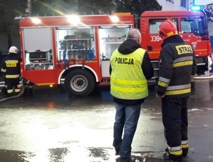 zdjęcie kolorowe: policjant i strażak stojący przed wozem bojowym straży pożarnej