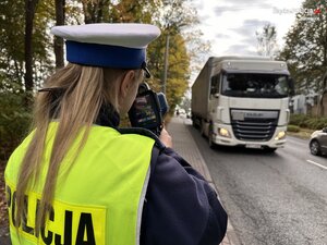zdjęcie kolorowe: przedstawiające policjantkę, która dokonuje pomiaru prędkości nadjeżdżającemu pojazdowi