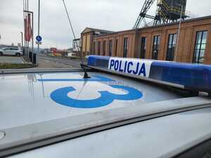 zdjęcie kolorowe: przedstawiające radiowóz policyjny na tle drogi i budynku