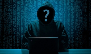 zdjęcie kolorowe: mężczyzna siedzący w kapturze założonym na głowę przed laptopem