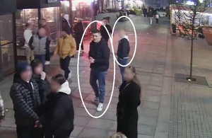 zdjęcie kolorowe: ulica na której znajdują się przechodnie i młody mężczyzna ubrany w czarna kurtkę, czarną bluzę, niebieskie spodnie i białe buty