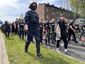 zdjęcie kolorowe: policjant i kibice idący drogą