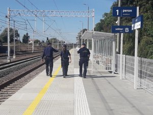 zdjęcie kolorowe: peron dworca kolejowego na którym stoi dwóch policjantów i strażnik ochrony kolei