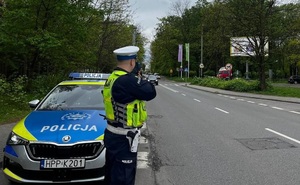 zdjęcie kolorowe: policjant ruchu drogowego kontrolujący prędkość pojazdów w rejonie oznakowanego przejścia dla pieszych