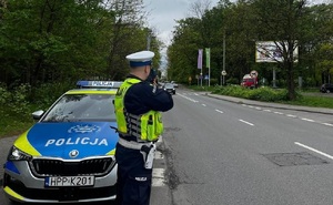 zdjęcie kolorowe: policjant ruchu drogowego kontrolujący prędkość pojazdów w rejonie oznakowanego przejścia dla pieszych