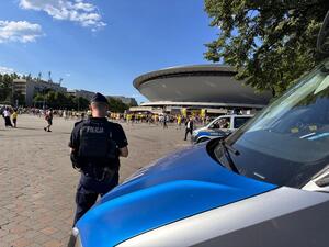 zdjęcie kolorowe przedstawiające umundurowanego policjanta wraz z radiowozem pod Spodkiem