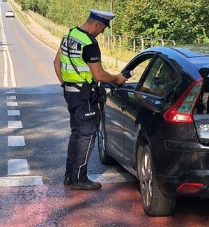 zdjęcie kolorowe: policjant ruchu drogowego kontrolujący stan trzeźwości kierującego samochodem