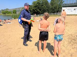 zdjęcie kolorowe: katowiccy policjanci i strażnicy miejscy rozmawiający z plażowiczami w Dolinie Trzech Stawów w Katowicach