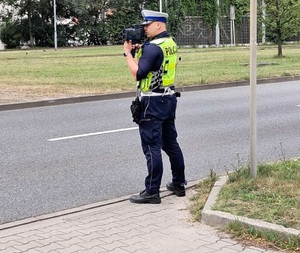 zdjęcie kolorowe: policjant katowickiej drogówki mierzący prędkość z jaką porusza się samochód