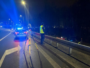 Na zdjęciu widoczny policjant, radiowóz oraz ambulans. Po prawej stronie widoczny samochód oraz parawan