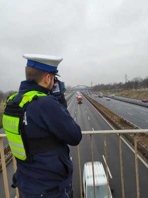 Na zdjęciu widoczny umundurowany policjant mierzący prędkość za pomocą miernika prędkości