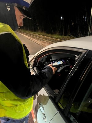 Na zdjęciu umudurowany policjant badający trzeźwość kierowcy