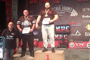 Na zdjęciu policjant na pierwszym stopniu podium oraz mężczyzna na drugim stopniu podium i trzeci mężczyzna stojący obok