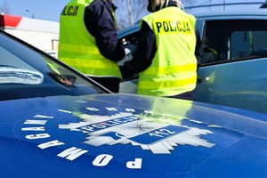 Na zdjęciu policyjny radiowóz z logiem pomagamy i chronimy oraz policjanci w kamizelkach odblaskowych