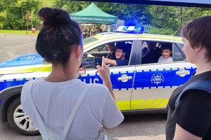 Na zdjęciu młodzież przy radiowozie robiąca zdjęcie
